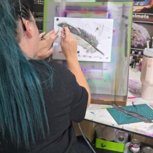 Student painting a feather design using masking and shading techniques